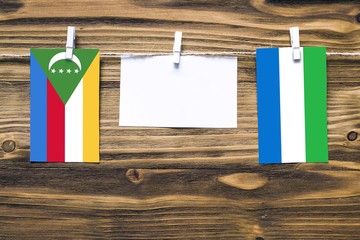 Hanging flags of Comoros and Sierra Leone attached to rope with clothes pins with copy space on...