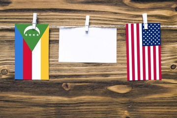 Hanging flags of Comoros and United States attached to rope with clothes pins with copy space on white note paper on wooden background.Diplomatic relations between countries.