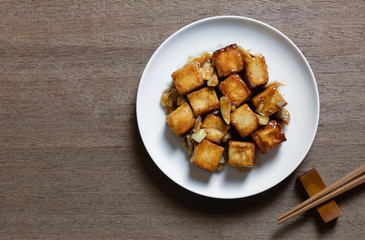 top view of stir fried fish tofu with oyster sauce in a ceramic dish on wooden table. asian homemade style food concept.