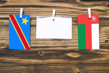 Hanging flags of Congo and Oman attached to rope with clothes pins with copy space on white note paper on wooden background.Diplomatic relations between countries.