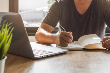 Close up view of hand holding a black luxury pen and writing on notebook diary.