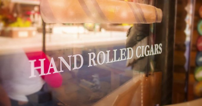 storefront video of small cigar shop with hand rolled cigars window graphics and an unrecognizable woman rolling cigars inside. Filmed in 4K RAW