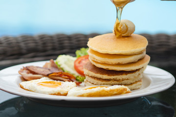 tasty breakfast in the morning. Piles of hot pancake pour honey on the top with bacon and fried eggs decorate with butter as breakfast dish.
