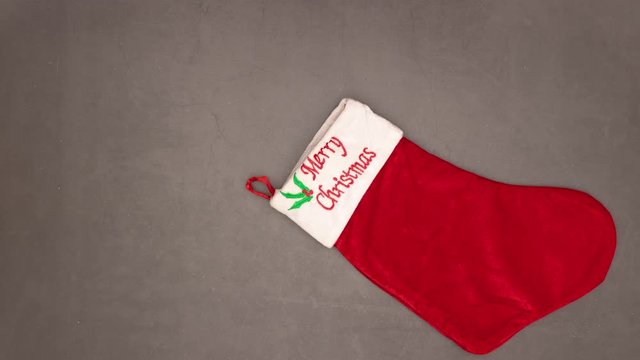 Christmas ornaments enter in Christmas sock on grey background - Stop motion 