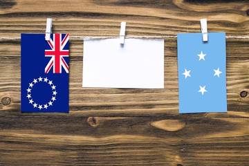 Hanging flags of Cook Islands and Micronesia attached to rope with clothes pins with copy space on white note paper on wooden background.Diplomatic relations between countries.