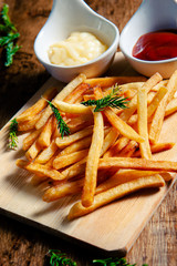 Crispy fry fries placed on a wooden chopping board with two dipping sauces, mayonnaise, tomato sauce