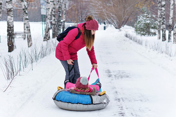 Active young mother rolls her baby on a snow tubing. Winter activities. Happiness to be a parent. Family look. 