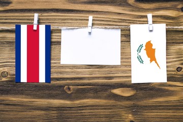 Hanging flags of Costa Rica and Cyprus attached to rope with clothes pins with copy space on white note paper on wooden background.Diplomatic relations between countries.