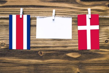 Hanging flags of Costa Rica and Denmark attached to rope with clothes pins with copy space on white note paper on wooden background.Diplomatic relations between countries.