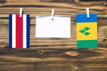 Hanging flags of Costa Rica and Saint Vincent And The Grenadines attached to rope with clothes pins with copy space on white note paper on wooden background.Diplomatic relations between countries.