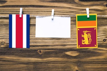 Hanging flags of Costa Rica and Sri Lanka attached to rope with clothes pins with copy space on white note paper on wooden background.Diplomatic relations between countries.