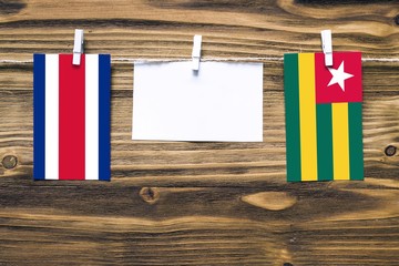 Hanging flags of Costa Rica and Togo attached to rope with clothes pins with copy space on white note paper on wooden background.Diplomatic relations between countries.