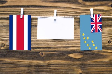 Hanging flags of Costa Rica and Tuvalu attached to rope with clothes pins with copy space on white note paper on wooden background.Diplomatic relations between countries.