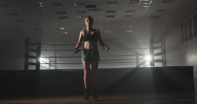 Caucasian female athlete training near a boxing ring, skipping on a rope, getting in shape before a fight - sports, motivation concept 4k footage