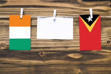 Hanging flags of Cote D'Ivoire and East Timor attached to rope with clothes pins with copy space on white note paper on wooden background.Diplomatic relations between countries.