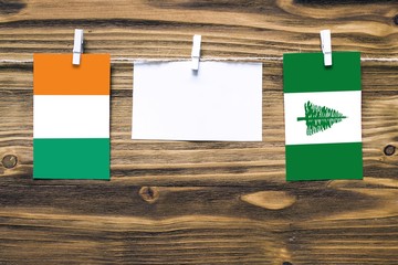 Hanging flags of Cote D'Ivoire and Norfolk Island attached to rope with clothes pins with copy space on white note paper on wooden background.Diplomatic relations between countries.