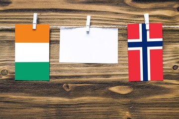 Hanging flags of Cote D'Ivoire and Norway attached to rope with clothes pins with copy space on white note paper on wooden background.Diplomatic relations between countries.