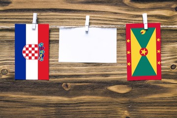 Hanging flags of Croatia and Grenada attached to rope with clothes pins with copy space on white note paper on wooden background.Diplomatic relations between countries.