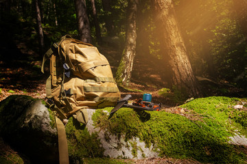 Hiker backpack with knife and flashlight in shady forest.