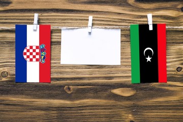 Hanging flags of Croatia and Libya attached to rope with clothes pins with copy space on white note paper on wooden background.Diplomatic relations between countries.