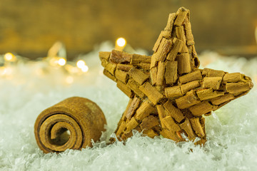 a cinnamon star lies on artificial snow with a string of lights in the background - 299677954