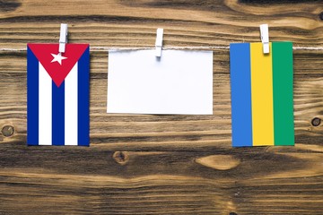 Hanging flags of Cuba and Gabon attached to rope with clothes pins with copy space on white note...