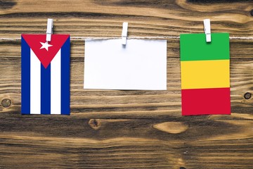 Hanging flags of Cuba and Mali attached to rope with clothes pins with copy space on white note paper on wooden background.Diplomatic relations between countries.