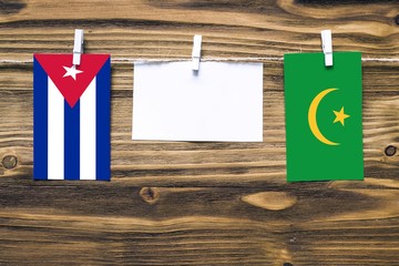 Hanging flags of Cuba and Mauritania attached to rope with clothes pins with copy space on white note paper on wooden background.Diplomatic relations between countries.