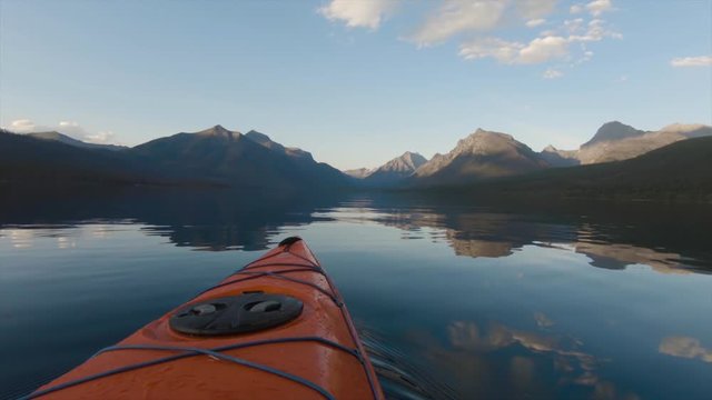 Kayaking in Lake McDonald during a sunny summer sunset with American Rocky Mountains in the background. Taken in Glacier National Park, Montana, USA.