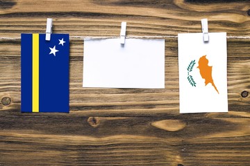 Hanging flags of Curacao and Cyprus attached to rope with clothes pins with copy space on white...