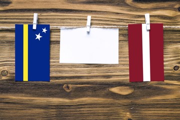 Hanging flags of Curacao and Latvia attached to rope with clothes pins with copy space on white note paper on wooden background.Diplomatic relations between countries.