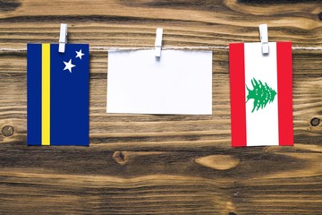 Hanging flags of Curacao and Lebanon attached to rope with clothes pins with copy space on white note paper on wooden background.Diplomatic relations between countries.