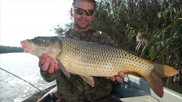 Happy angler holds trophy carp (Cyprinus carpio) looks at the camera and smiles