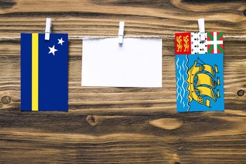 Hanging flags of Curacao and Saint Pierre And Miquelon attached to rope with clothes pins with copy...