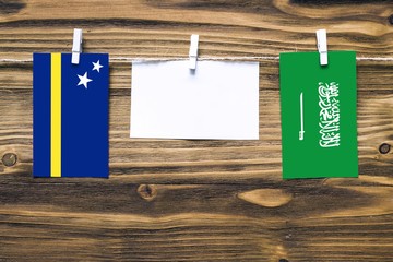 Hanging flags of Curacao and Saudi Arabia attached to rope with clothes pins with copy space on white note paper on wooden background.Diplomatic relations between countries.
