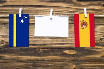 Hanging flags of Curacao and Spain attached to rope with clothes pins with copy space on white note paper on wooden background.Diplomatic relations between countries.