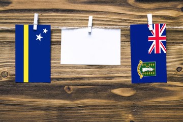 Hanging flags of Curacao and British Virgin Islands attached to rope with clothes pins with copy space on white note paper on wooden background.Diplomatic relations between countries.