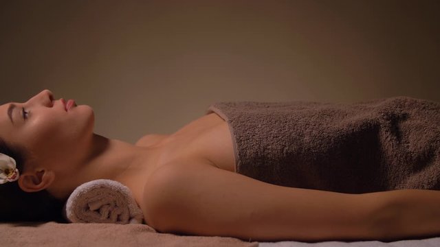 wellness, beauty and relaxation concept - young woman lying at spa or massage parlor with burning aromatic candle