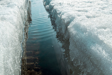 A wide crack in the ice, melting ice. The field of ice cover disintegrates, becomes loose and the dark water surface is exposed.