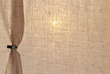 Cotton curtains with vintage clothespin. Horizontal view. The sun shines through a golden beige curtain of cotton fabric without a pattern, secured with an old clothespin.