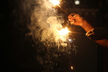 human Hand holding the sparkler on sparkling with dark background with some white smoke on the deepavali / dewali celebration