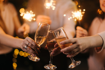 Close-up of glasses of clinking Champagne with Bengali lights. Celebration concept - obrazy, fototapety, plakaty