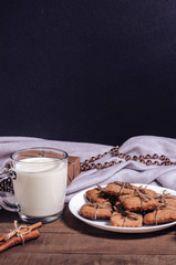 A cup of milk, cinnamon sticks and homemade cookies in a Christmas decor.