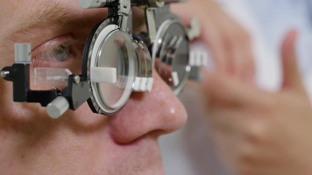 Tilt up shot with extreme close up of unrecognizable optometrist changing lenses on trial frame worn by male patient during eye exam