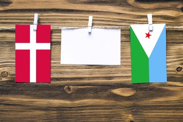 Hanging flags of Denmark and Djibouti attached to rope with clothes pins with copy space on white note paper on wooden background.Diplomatic relations between countries.