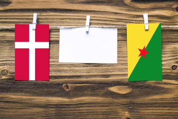 Hanging flags of Denmark and French Guiana attached to rope with clothes pins with copy space on white note paper on wooden background.Diplomatic relations between countries.