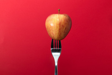 Juicy red apple that has been stuck on the end of a fork in front of a vibrant red background