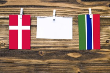 Hanging flags of Denmark and Gambia attached to rope with clothes pins with copy space on white note paper on wooden background.Diplomatic relations between countries.