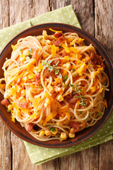 Spaghetti with bacon, corn and cheese  Mimolette close-up on a plate. Vertical top view