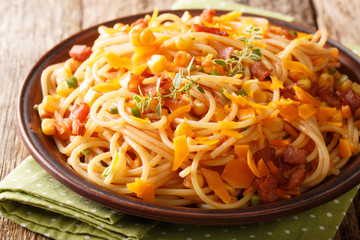 Spaghetti pasta salad with bacon, corn and Mimolette cheese close-up on a plate on the table. horizontal